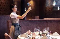 Kellnerin im Dirndl hebt Weinglas in elegantem Restaurant mit gedecktem Tisch